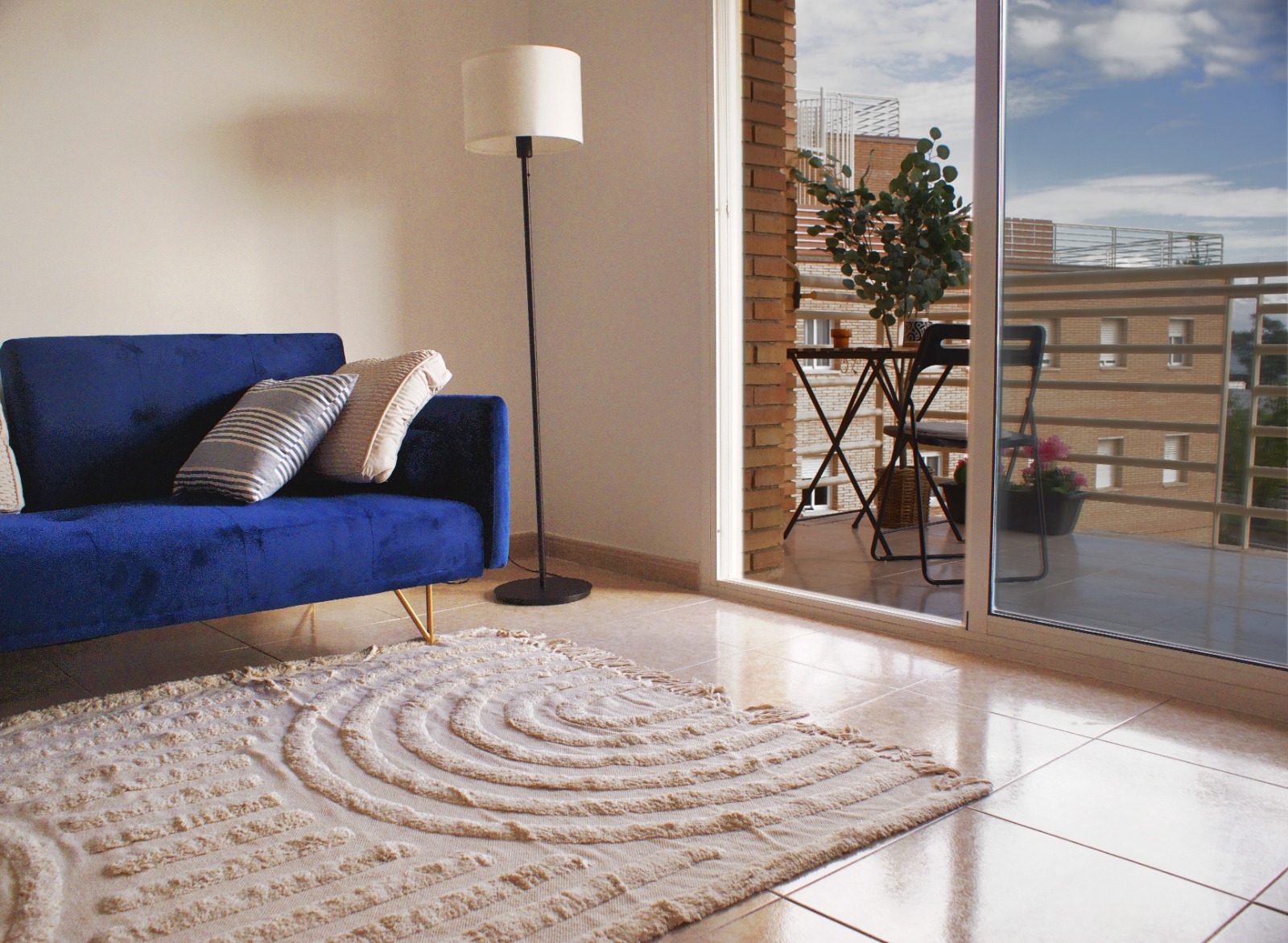 salon son sofa azul y alfombra color crema y un balcon con zona de estar